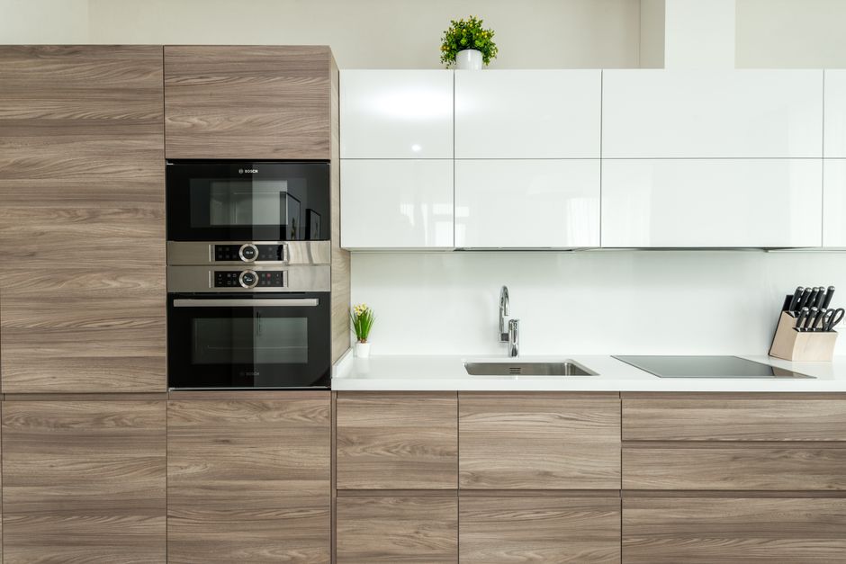 A modern kitchen featuring a combination of natural wood grain cabinets and sleek white upper cabinets. A built-in oven and microwave are integrated into the wooden cabinetry on the left. The countert